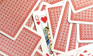 A deck of playing cards with red backs spread out with a single queen face up in the centre