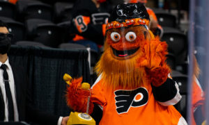 Gritty holds a old-fashioned yellow rotary phone while waving to the camera