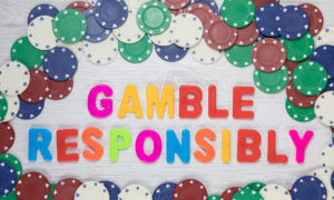 Assorted denominations of casino chips seen from above form a frame around colourful text reading gamble responsibly