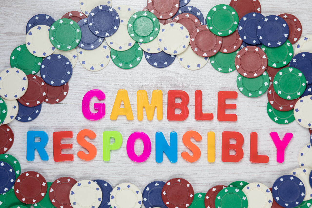 Assorted denominations of casino chips seen from above form a frame around colourful text reading gamble responsibly