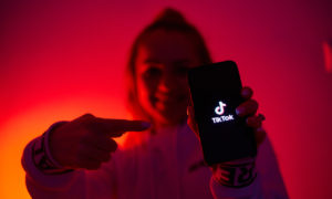 A woman, awash red, points to a phone screen showing the tiktok logo