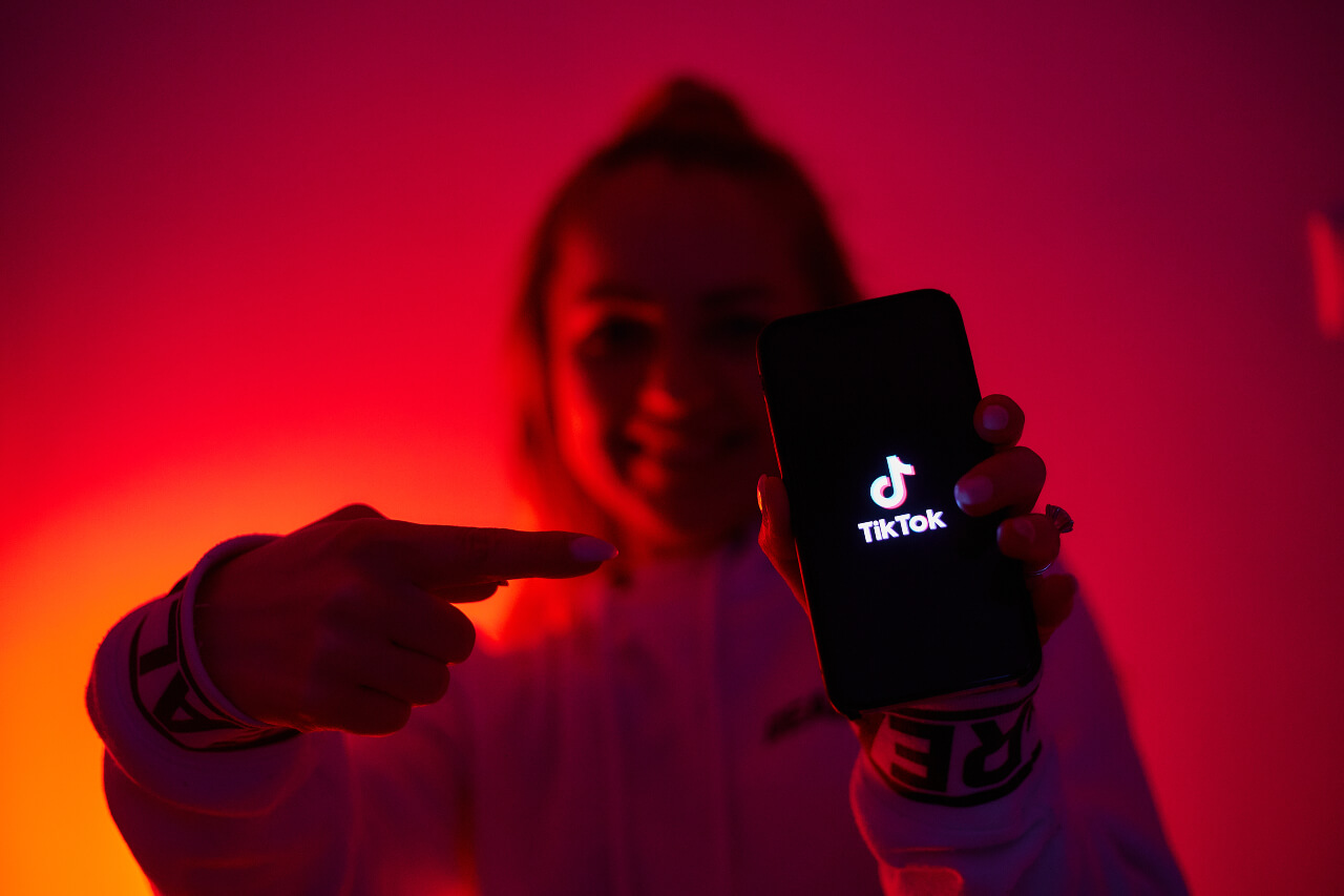 A woman, awash red, points to a phone screen showing the tiktok logo