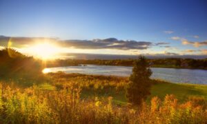 The sun sets on Nova Scotia Gaming Coporation. A beautiful sunset over river with autumn trees in foreground in Sydney, NS