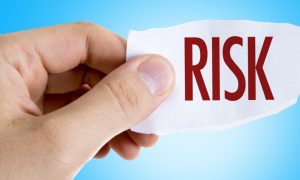 A hand holding a torn piece of paper with the word "RISK" printed in bold red letters against a light blue background