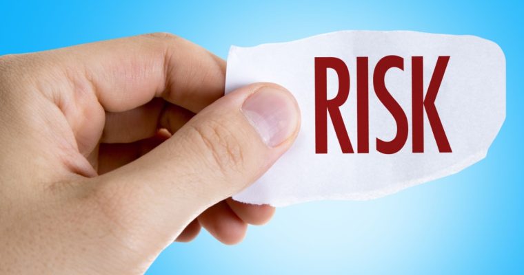 A hand holding a torn piece of paper with the word "RISK" printed in bold red letters against a light blue background